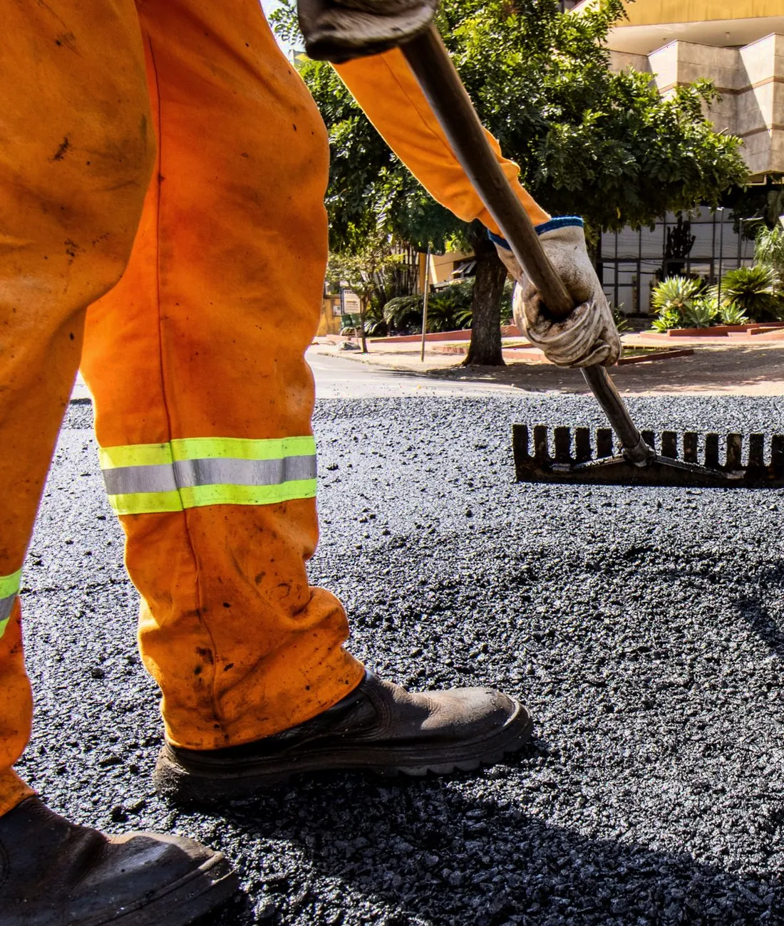 Paving crew member raking a fresh, steaming asphalt mat smooth
