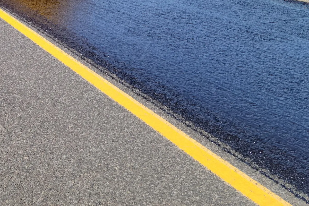 Close-up of fresh, wet black sealcoat beside a crisp yellow line